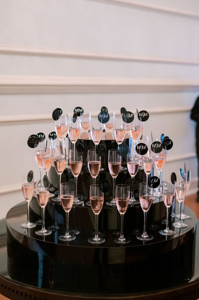 Flutes holding pink rose sit on a four-tiered black display | Wedding Photography by Lauren Bliss at the Cescaphe Ballroom Philadelphia