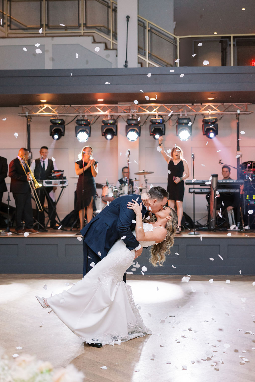 Groom dips bride to kiss her in front of a live band under a shower of white flower petals | Lauren Bliss Wedding Photography in Philadelphia