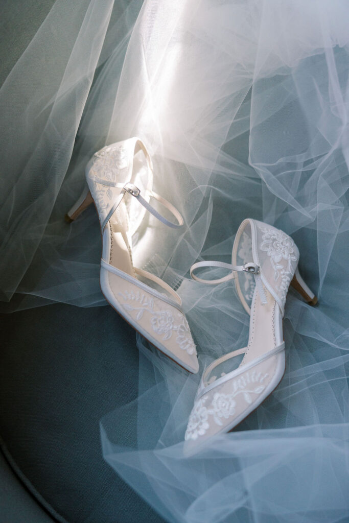 Bella Belle lace wedding shoes sit on top a tulle veil under a shaft of sunlight 