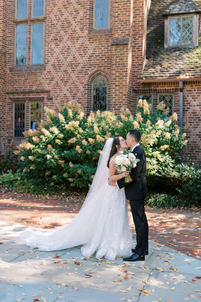 Couple kisses in front of white hydrangea bush at Aldie Mansion on their wedding day | Lauren Bliss Photography