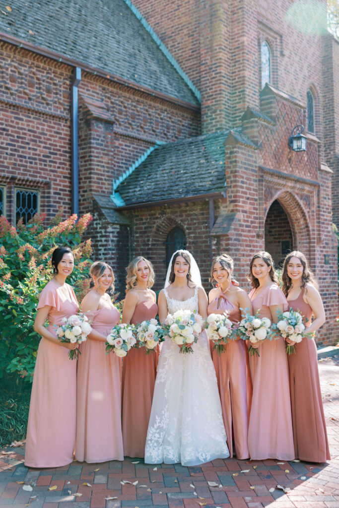 Bride stands with six bridesmaids wearing different shades of pink gowns | Lauren Bliss Photography