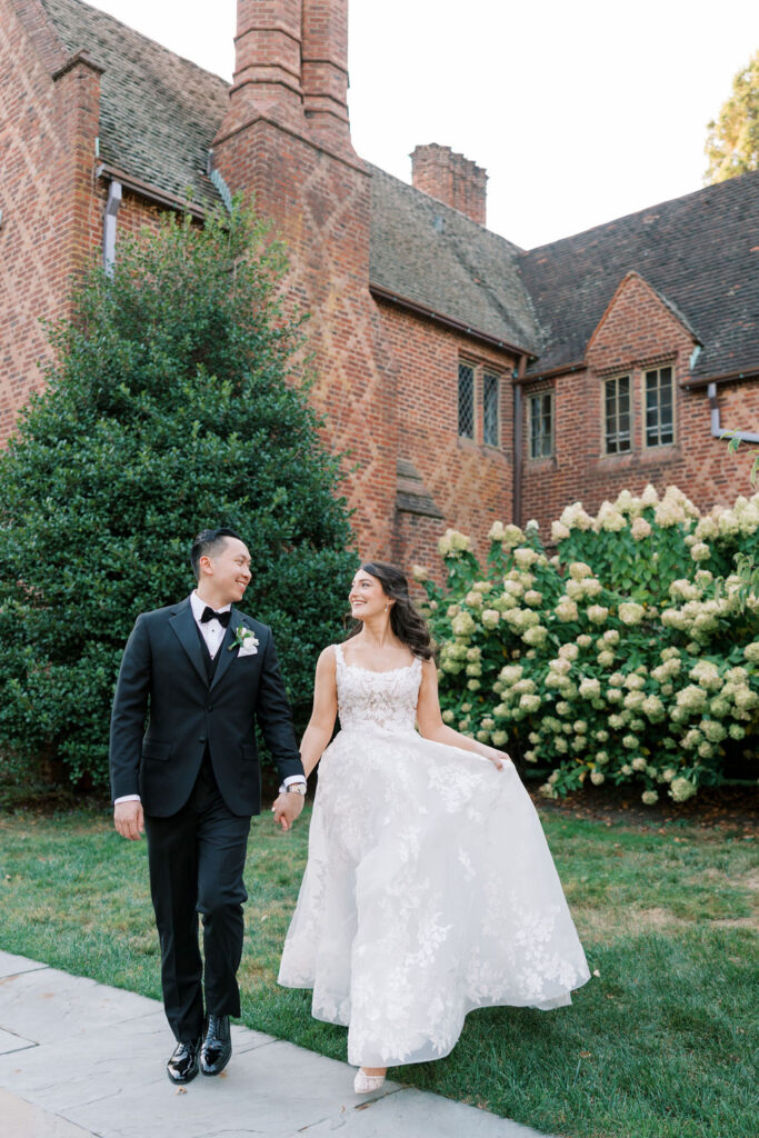 Couple walks hand in hand in front of white hydrangea bush at Aldie Mansion on their wedding day | Lauren Bliss Photography