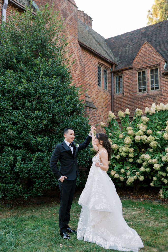 Couple twirls hand in hand in front of white hydrangea bush at Aldie Mansion on their wedding day | Lauren Bliss Photography