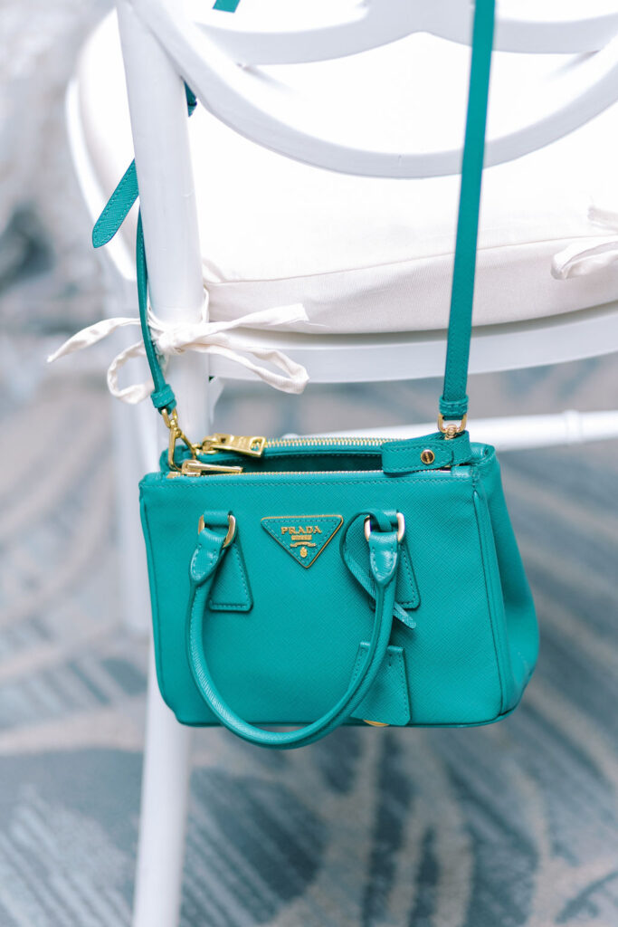 Teal blue Prada purse hangs on white chair at wedding reception | Lauren Bliss Photography at Lancaster Country Club