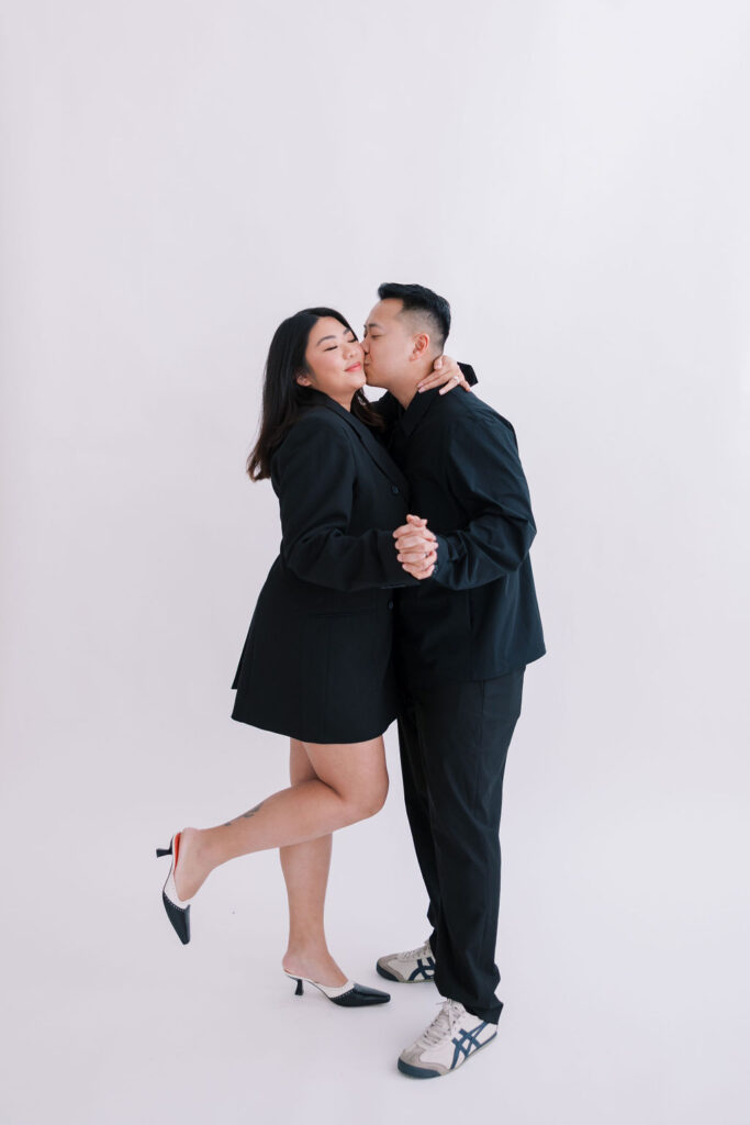 Man and woman wearing all black outfits pose in a photo studio against a white backdrop during their Philadelphia engagement session | Lauren Bliss Photography