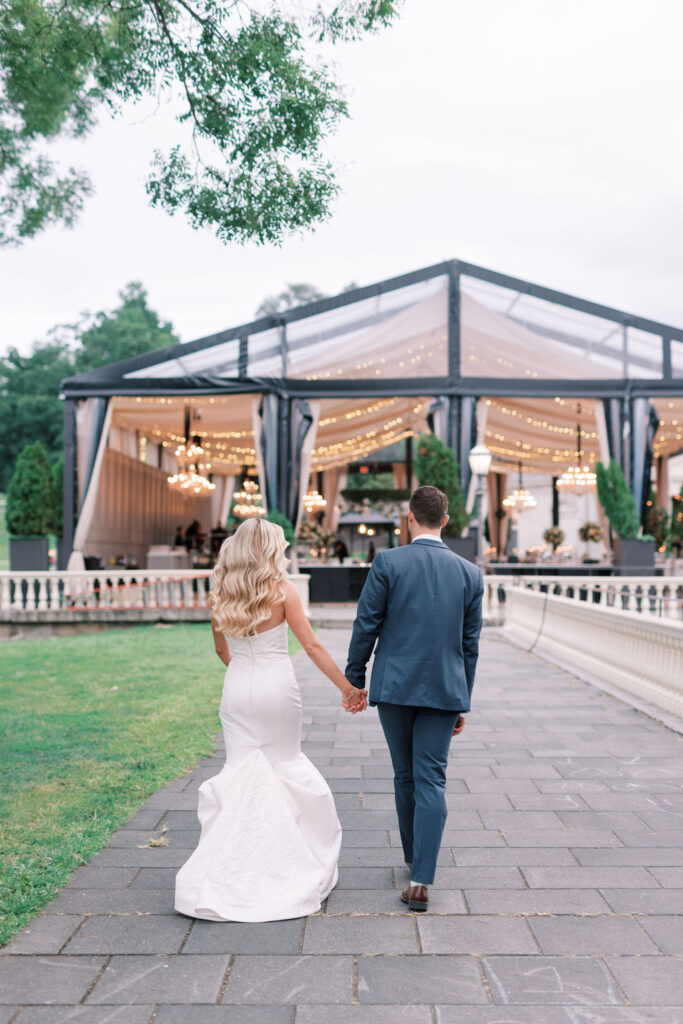 Bride and groom walk hand in hand into tented outdoor wedding venue | Philadelphia Wedding at Waterworks Cescaphe by Lauren Bliss Photography