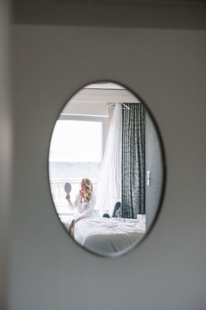 Bride sits on bed and looks into handheld mirror | Philadelphia Wedding at Waterworks Cescaphe by Lauren Bliss Photography