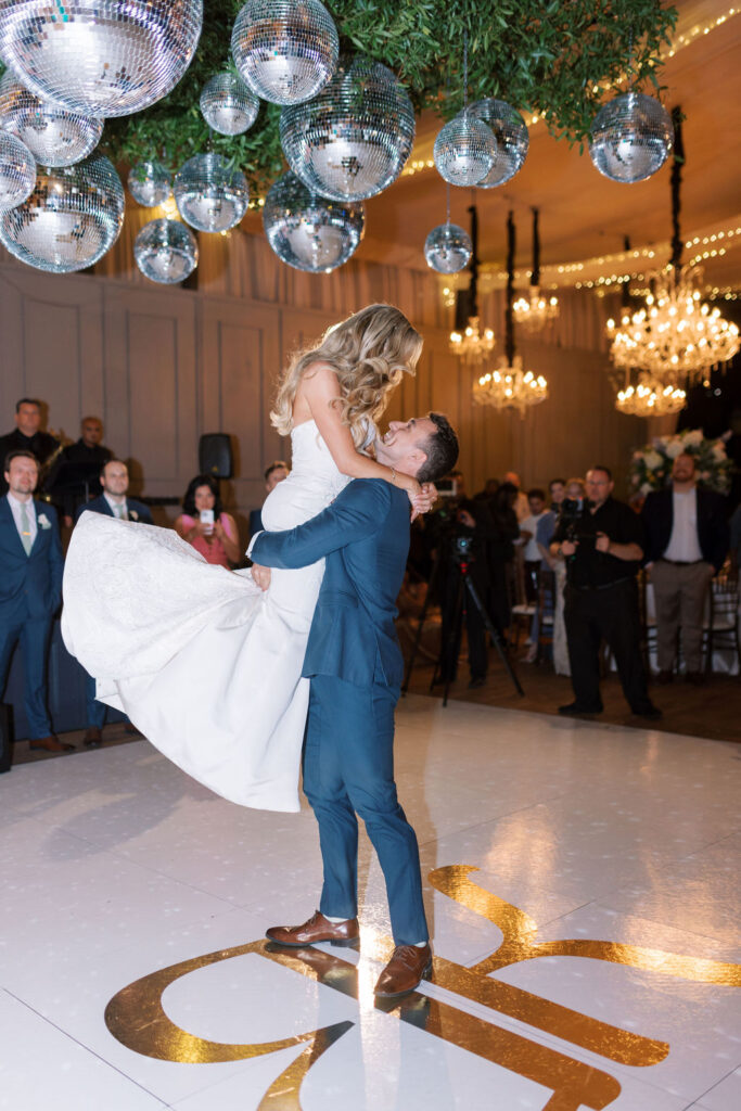 Groom lifts up bride on the dance floor underneath disco balls | Philadelphia Wedding at Waterworks Cescaphe by Lauren Bliss Photography