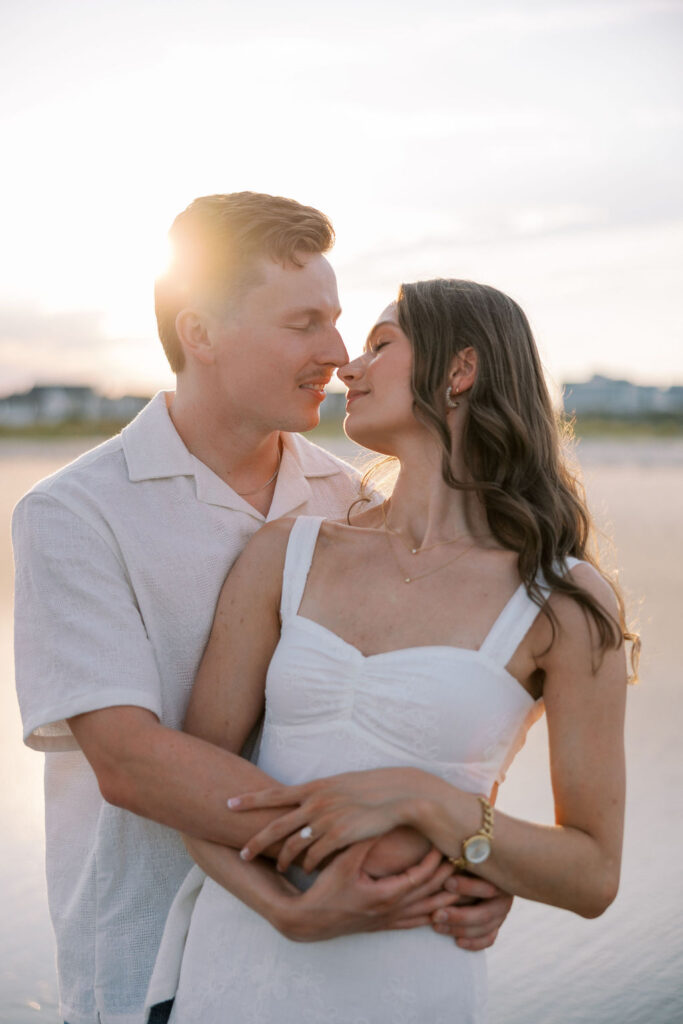 Woman in a white dress leans in to kiss her fiance during golden hour engagement portraits at Ocean City, NJ beach taken by Lauren Bliss Photography, full of warmth and romance
