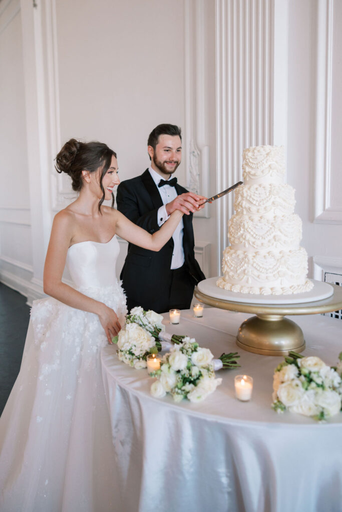 Bride and groom cut a white four tiered wedding cake together