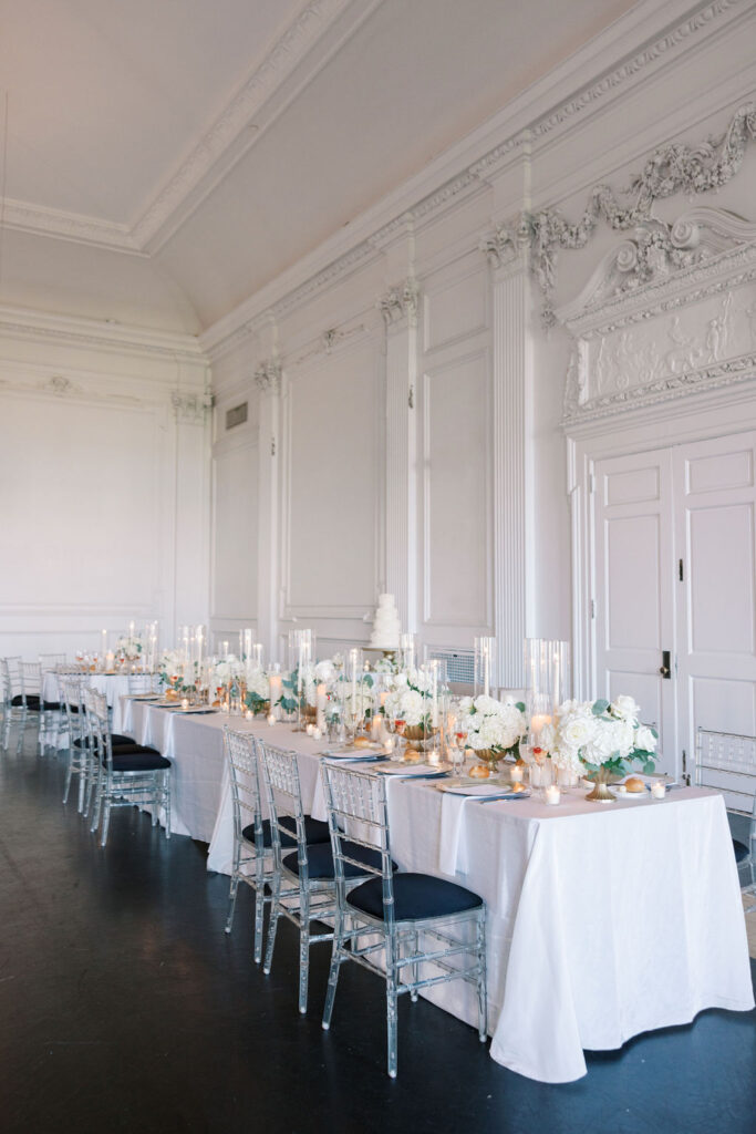 Reception banquet table covered in white linen and wedding floral centerpieces sits in front of grand double doors in the Cescaphe Down Town Club venues in Philadelphia