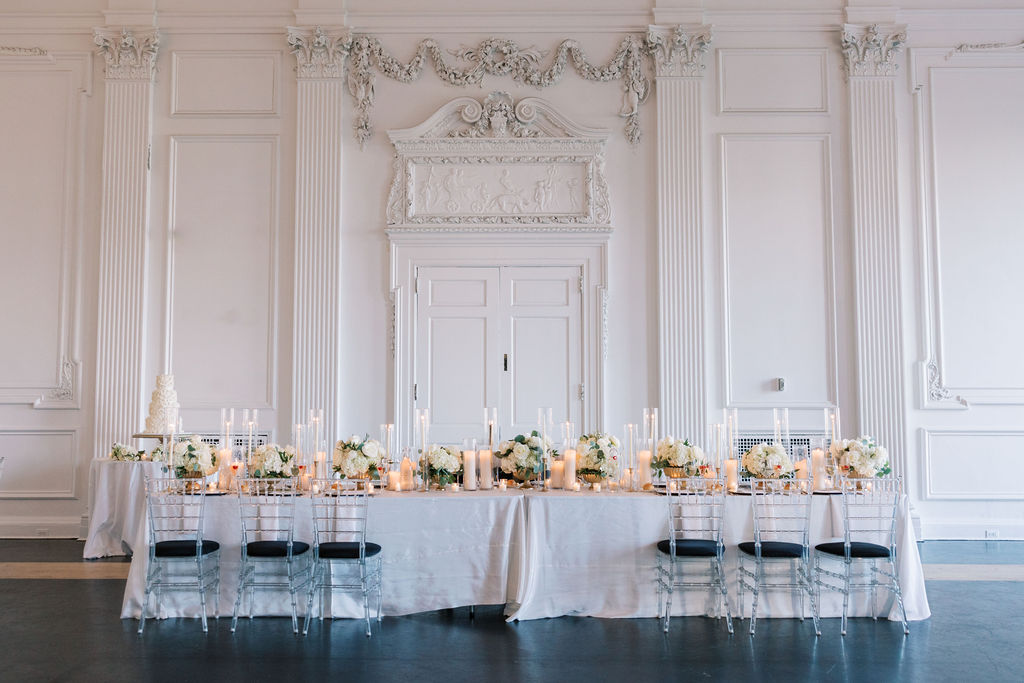 Reception banquet table covered in white linen and wedding floral centerpieces sits in front of grand double doors in the Cescaphe Down Town Club venues in Philadelphia