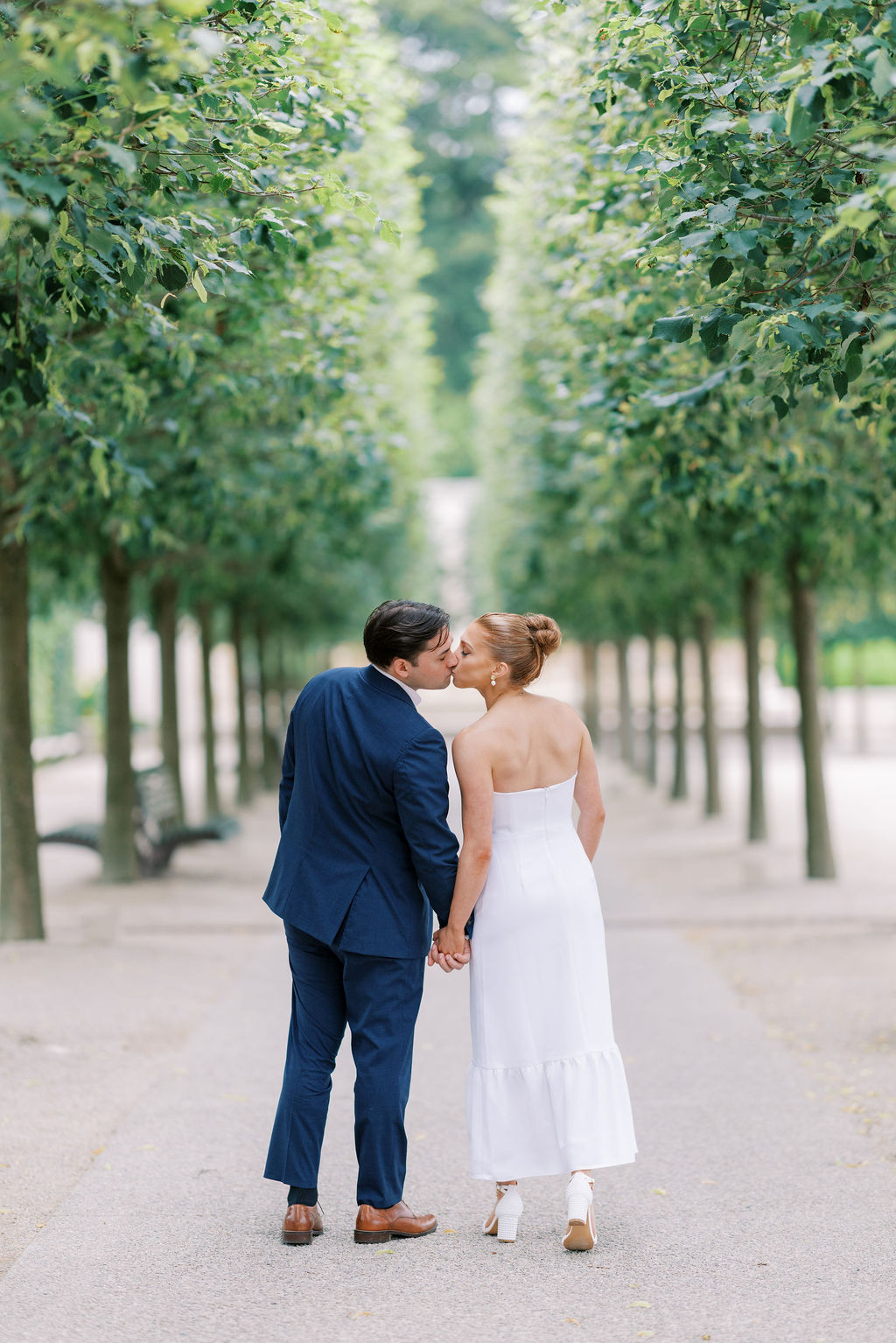 Stylish and heartfelt Longwood Gardens engagement portrait of couple kissing in front of a row of manicured trees by Lauren Bliss Photography, perfect for announcing your engagement on social media