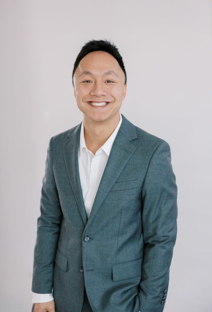 Portrait of a male photographer wearing a charcoal gray suit standing in front of a white backdrop in a photography studio
