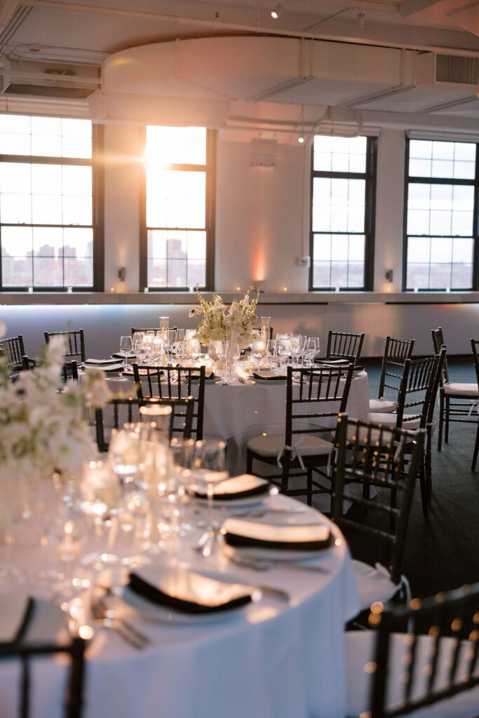 Elegant wedding reception tables with white floral centerpieces glowing in sunset light at Tribeca 360 rooftop venue in New York City.