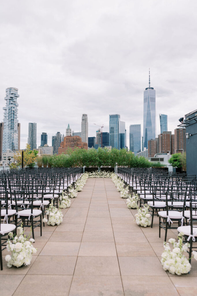 Rooftop wedding ceremony setup with white florals and Manhattan skyline views, including One World Trade Center, at Tribeca 360 in NYC.