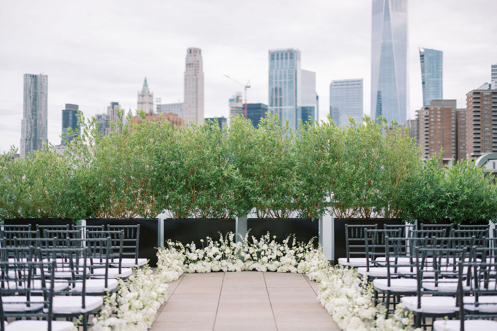 Wedding altar lined with white flowers and NYC skyscraper views at Tribeca 360 rooftop wedding venue in downtown Manhattan.