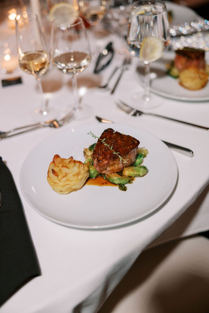 Plated dinner of filet mignon with brussels sprouts and potatoes at luxury wedding reception at Tribeca Rooftop, New York City.