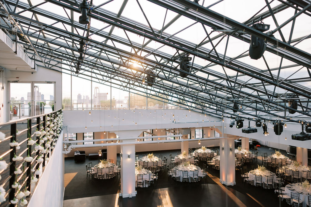 Panoramic view of Tribeca 360’s modern reception ballroom with glass ceiling, white florals, and elegant tables in Manhattan, NYC.