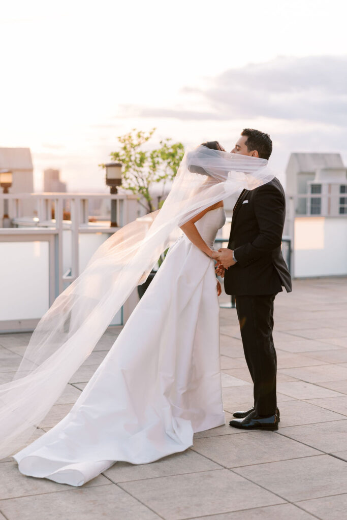 Romantic sunset rooftop wedding kiss with the bride’s veil blowing in the wind, captured at Tribeca 360 in NYC by luxury wedding photographer Lauren Bliss.