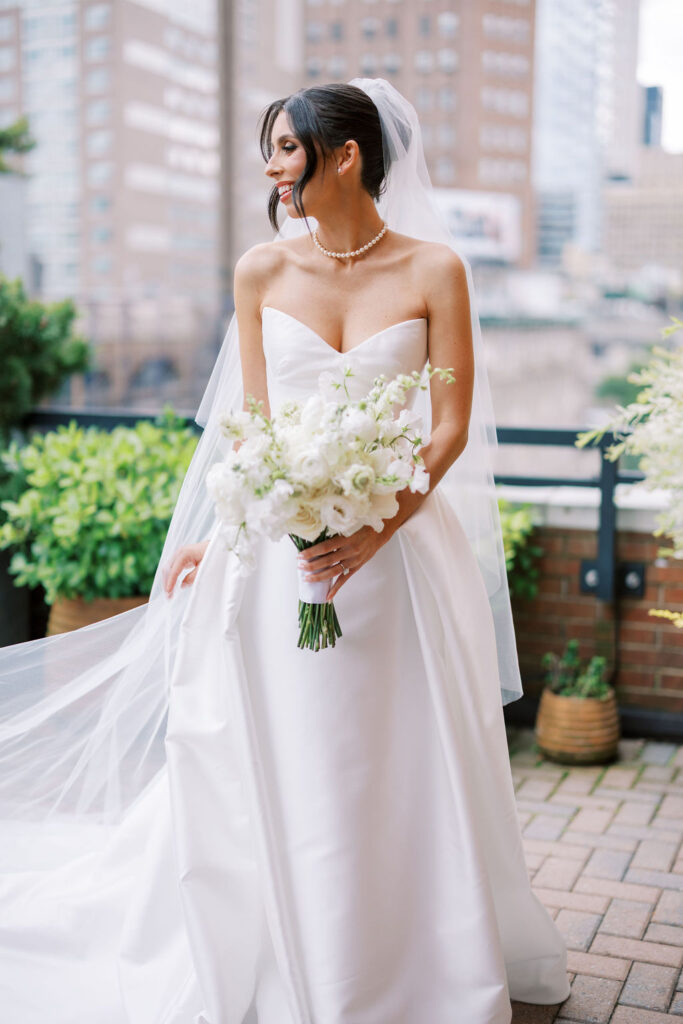 Bride smiling with her white bouquet and flowing veil on the terrace of Tribeca Rooftop in Manhattan, photographed by Lauren Bliss Photography.