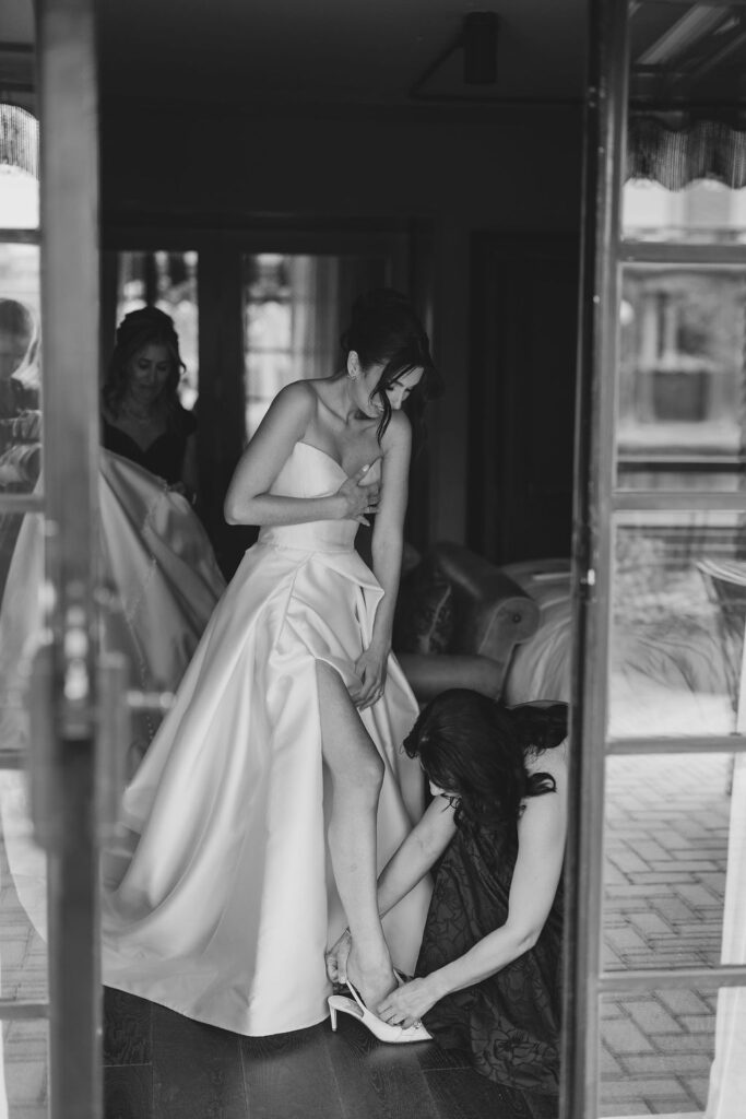 Bride in satin gown having her shoes fastened while getting ready for her Tribeca Rooftop wedding in New York City, captured by Lauren Bliss Photography.