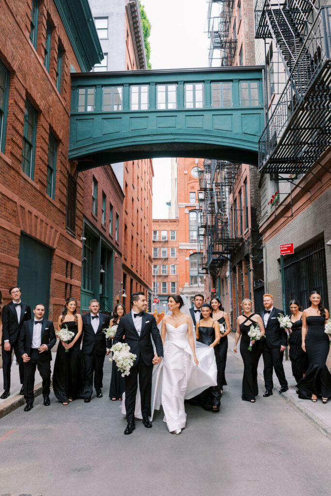Elegant wedding party walking through Tribeca streets under iconic pedestrian bridge in NYC, photographed by Lauren Bliss Photography