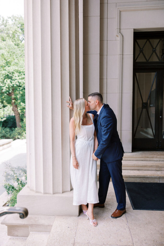 A romantic kiss between Kelsey and Lee under the grand columns of the Rodin Museum, blending timeless architecture with sweet intimacy