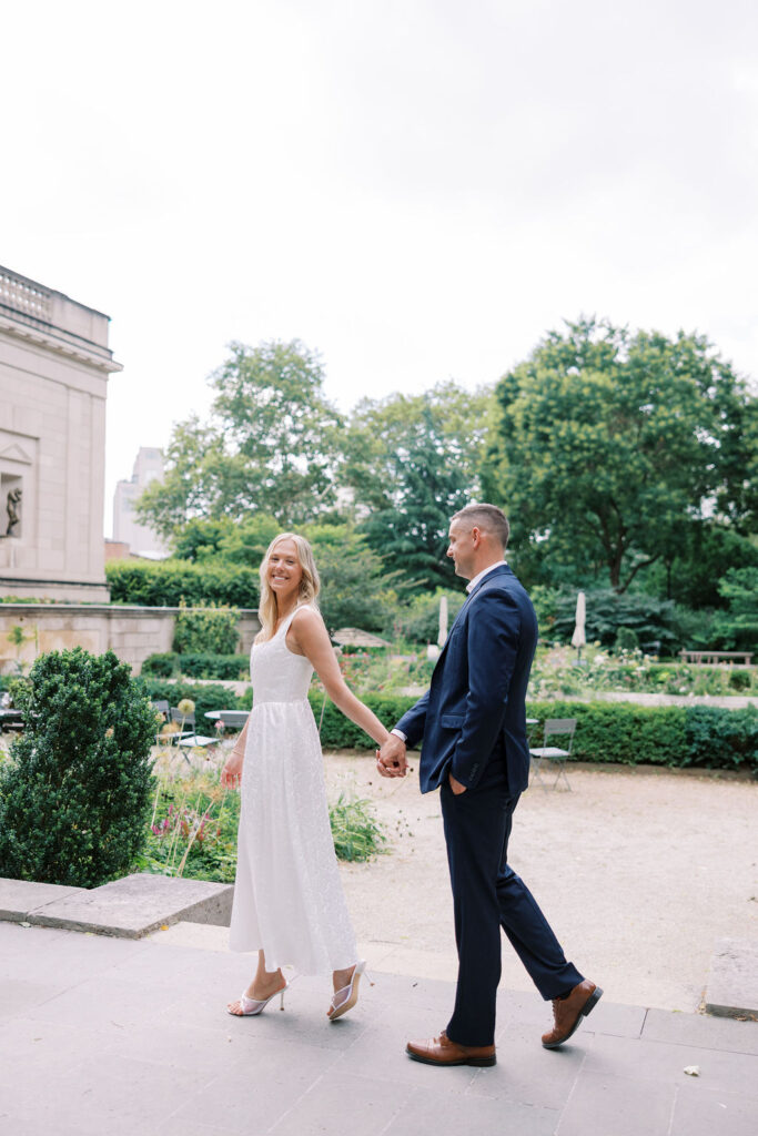 Elegant couple smiling and walking through the Rodin Museum garden courtyard during their Philadelphia engagement session with Lauren Bliss Photography