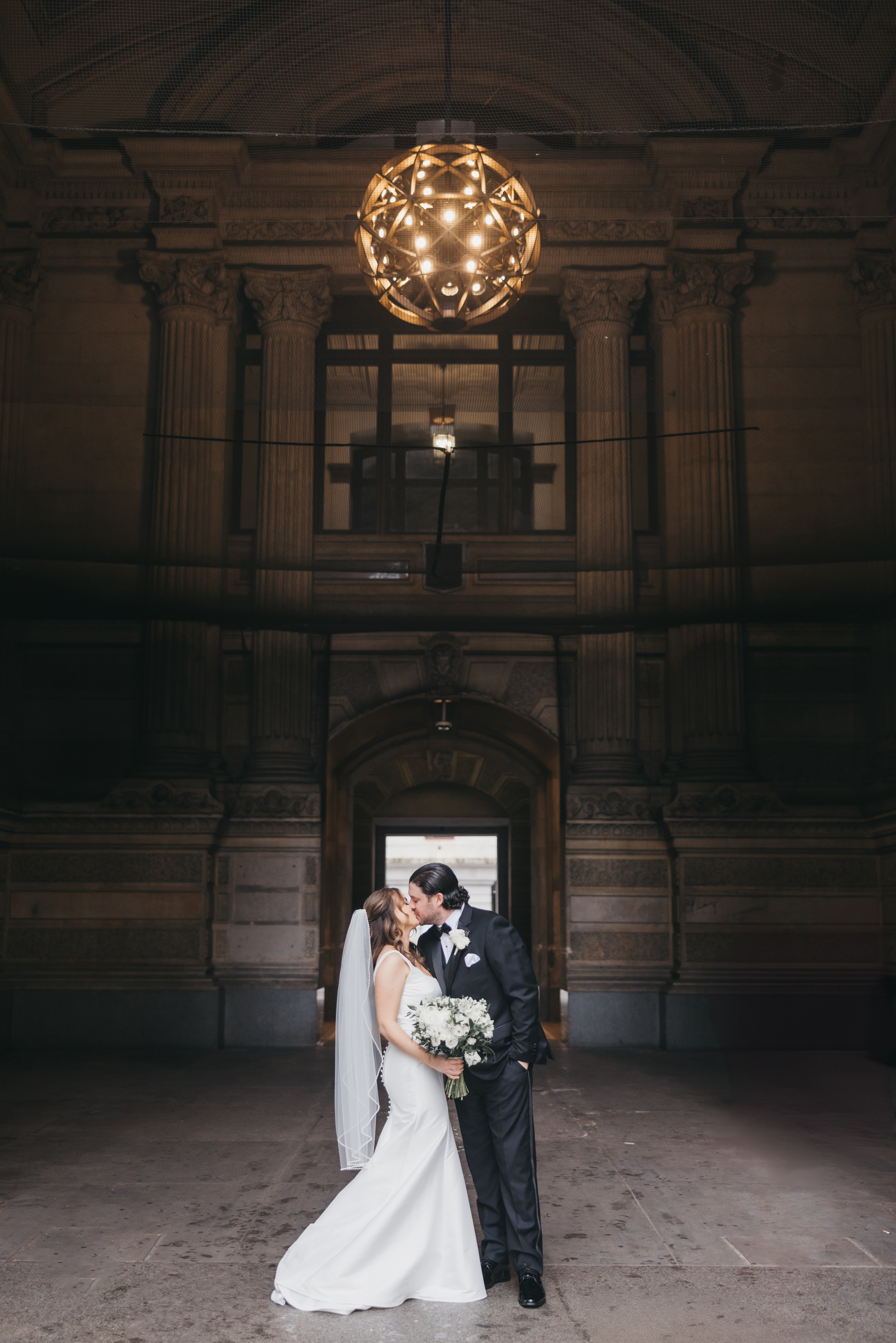 Bride and groom kissing under the grand illuminated archway of Philadelphia City Hall, captured by Lauren Bliss Photography.