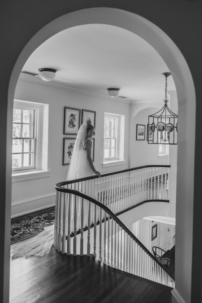 Bride walking along the interior staircase at Pomme, framed by arched architecture and window light, captured in a classic black and white bridal portrait by Lauren Bliss Photography.
