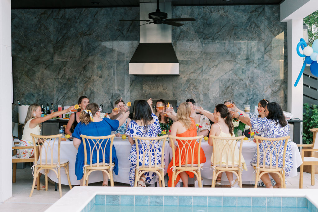 Guests raising Aperol cocktails for a toast at a long dinner table during a coastal 30A beach retreat.