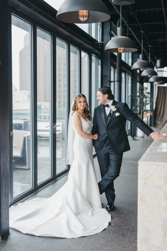 Bride and groom standing by floor-to-ceiling windows inside The Logan Hotel penthouse, captured during elegant wedding portraits by Lauren Bliss Photography.