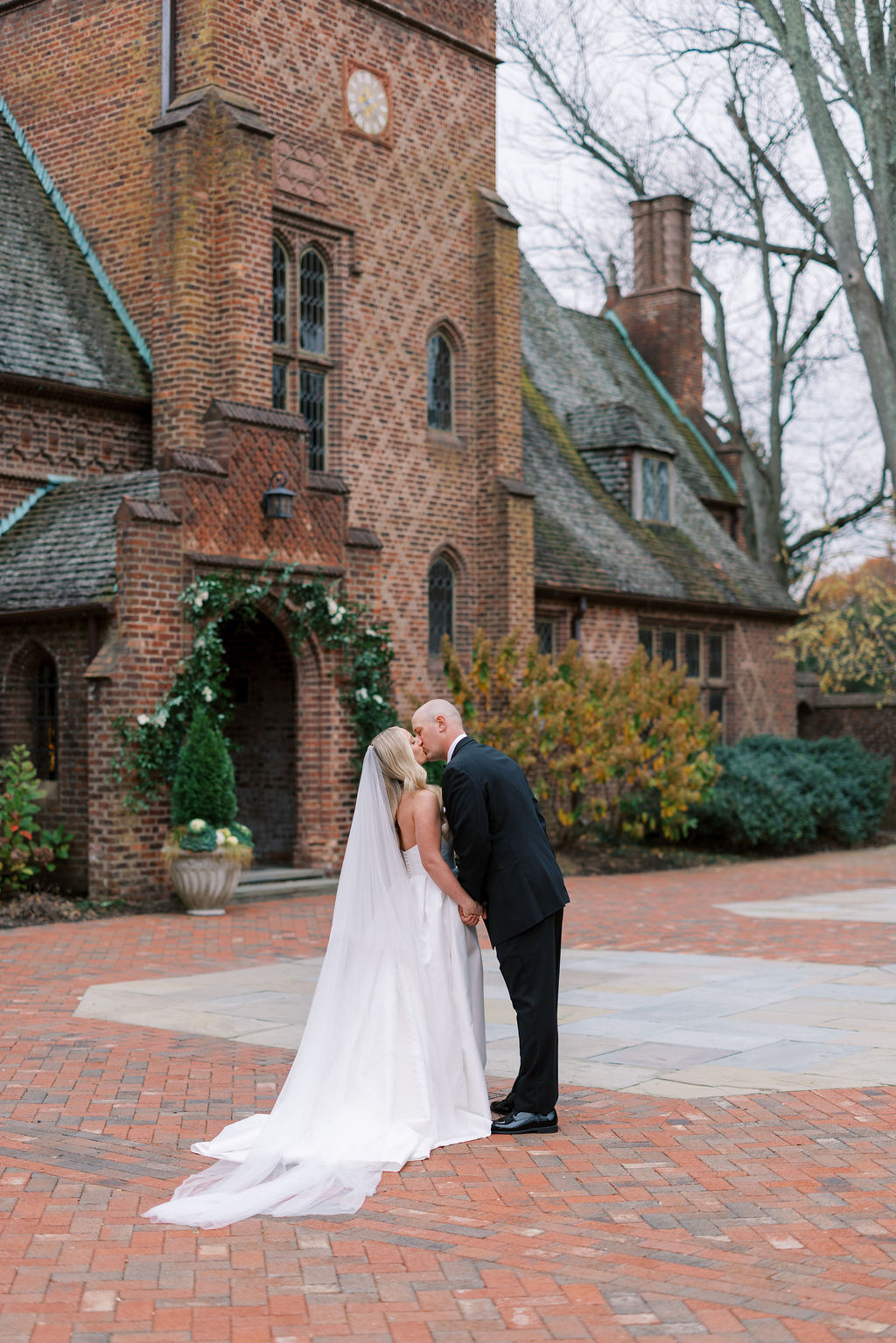 Bride and groom kiss in a brick courtyard in front of a English Tudor style brick wedding venue, Aldie Mansion, in Doylestown, PA.