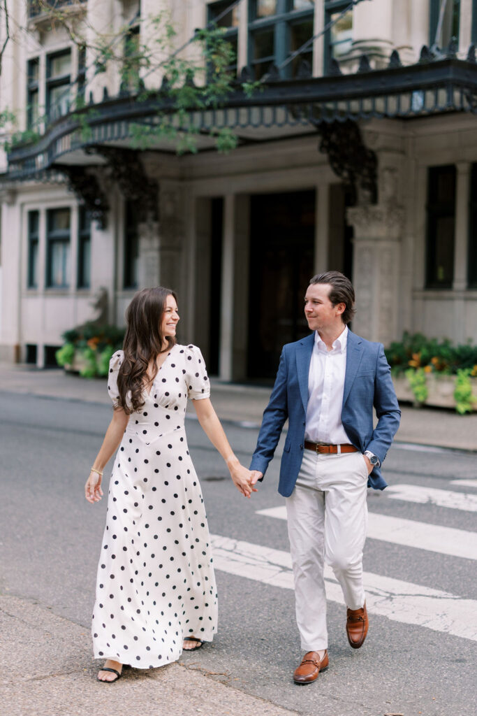 Couple holds hands and crosses street in front of 1830 Rittenhouse Square building in Philadelphia