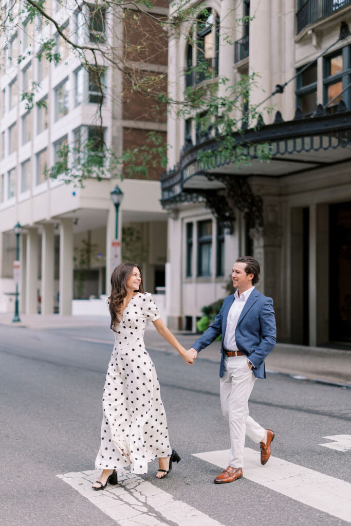 Couple holds hands, laughing and crosses street in front of 1830 Rittenhouse Square building in Philadelphia
