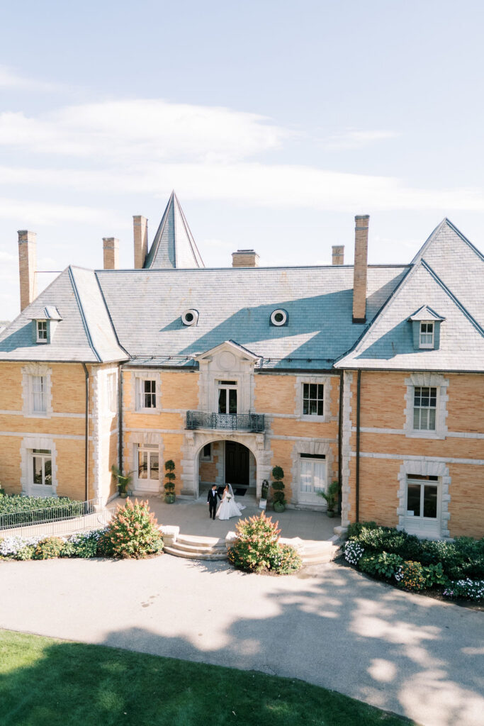 Aerial view of bride and groom at the mansion's arched entrance courtyard at a wedding at Cairnwood Estate