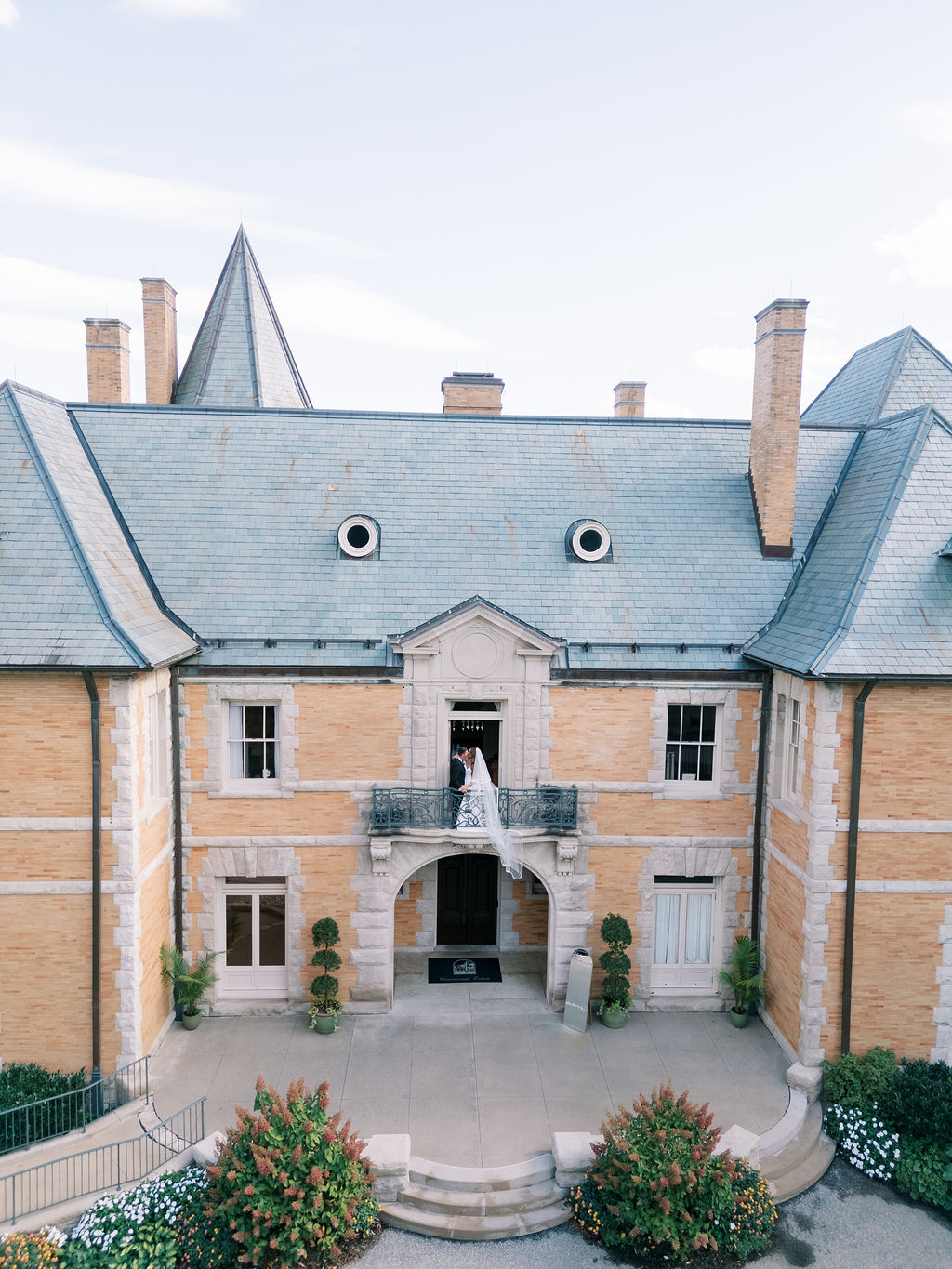 Aerial view of bride and groom on the wrought-iron balcony of the mansion at a wedding at Cairnwood Estate