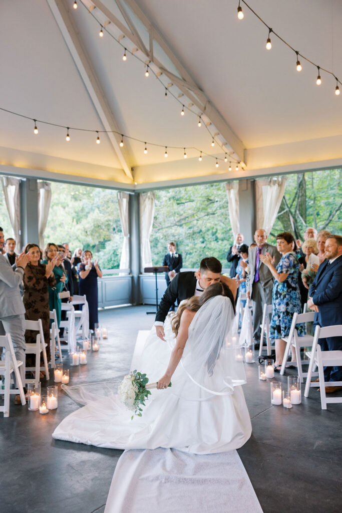 Bride and groom's dip kiss at the end of the aisle as guests applaud at a Cairnwood Estate wedding