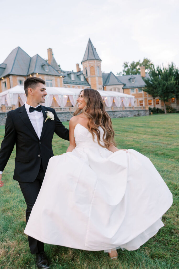 Bride and groom walking on the lawn at dusk with the mansion and terrace tent behind them at Cairnwood Estate