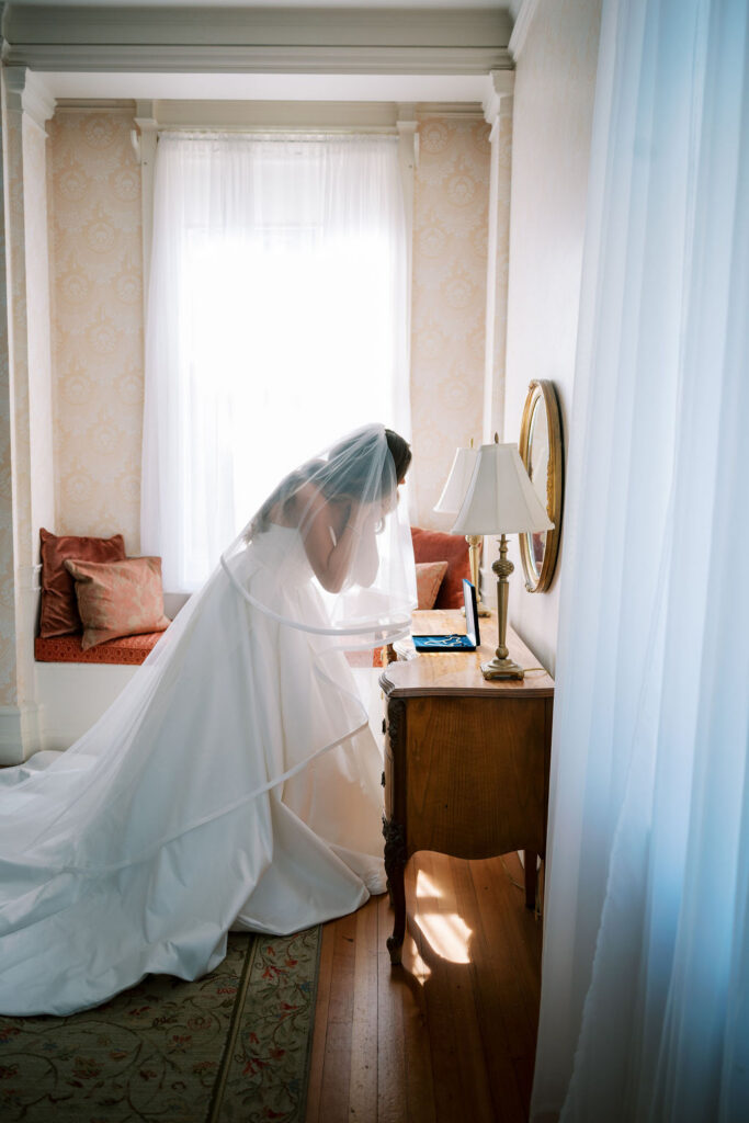 Bride in ballgown and two tier cathedral veil by a sunlit window at a wedding at Cairnwood Estate