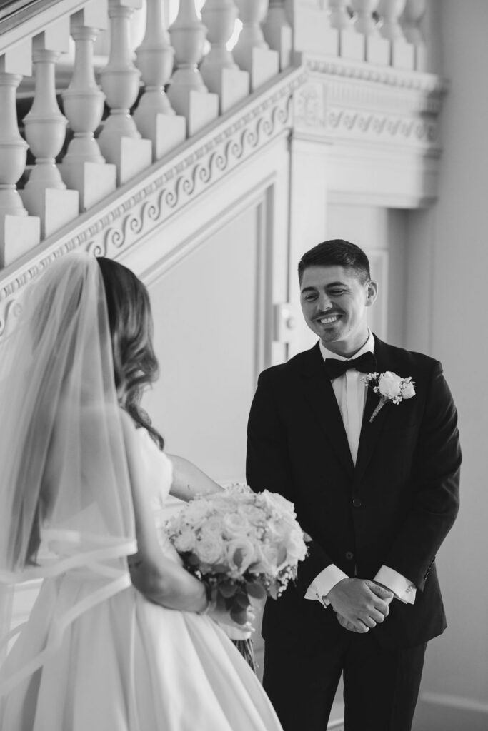Black and white first look on the grand staircase at a wedding at Cairnwood Estate in Bryn Athyn, PA