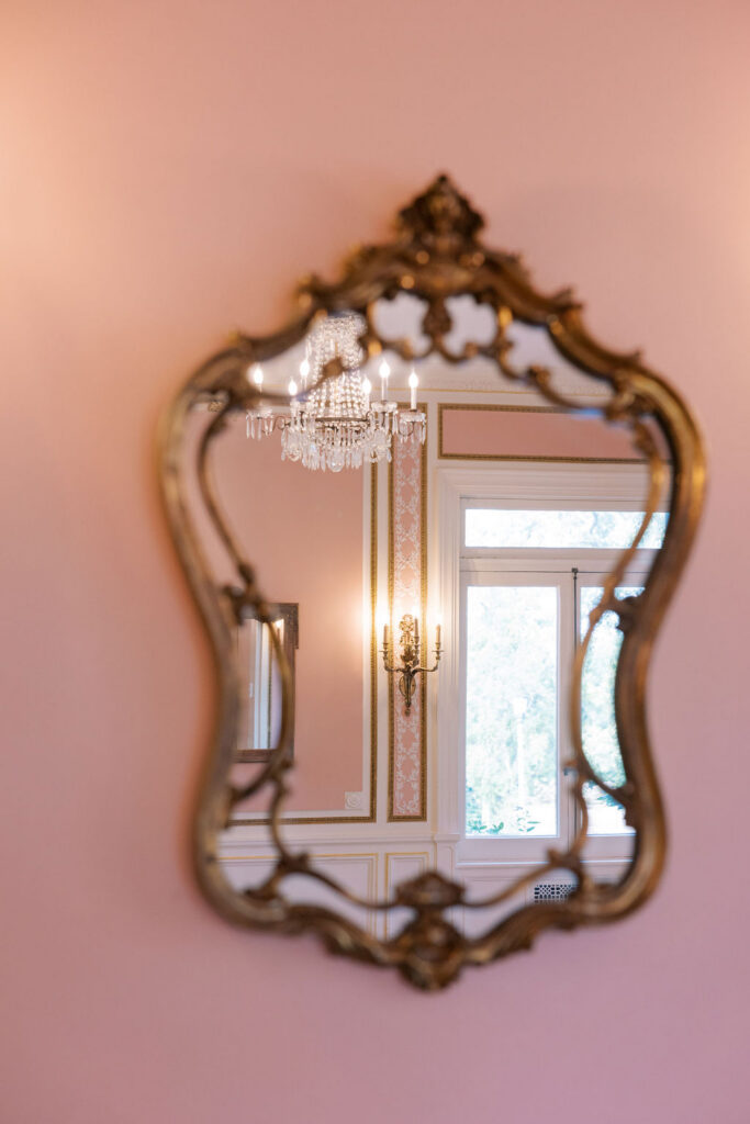 Ornate gilded mirror reflecting a chandelier in the blush bridal suite