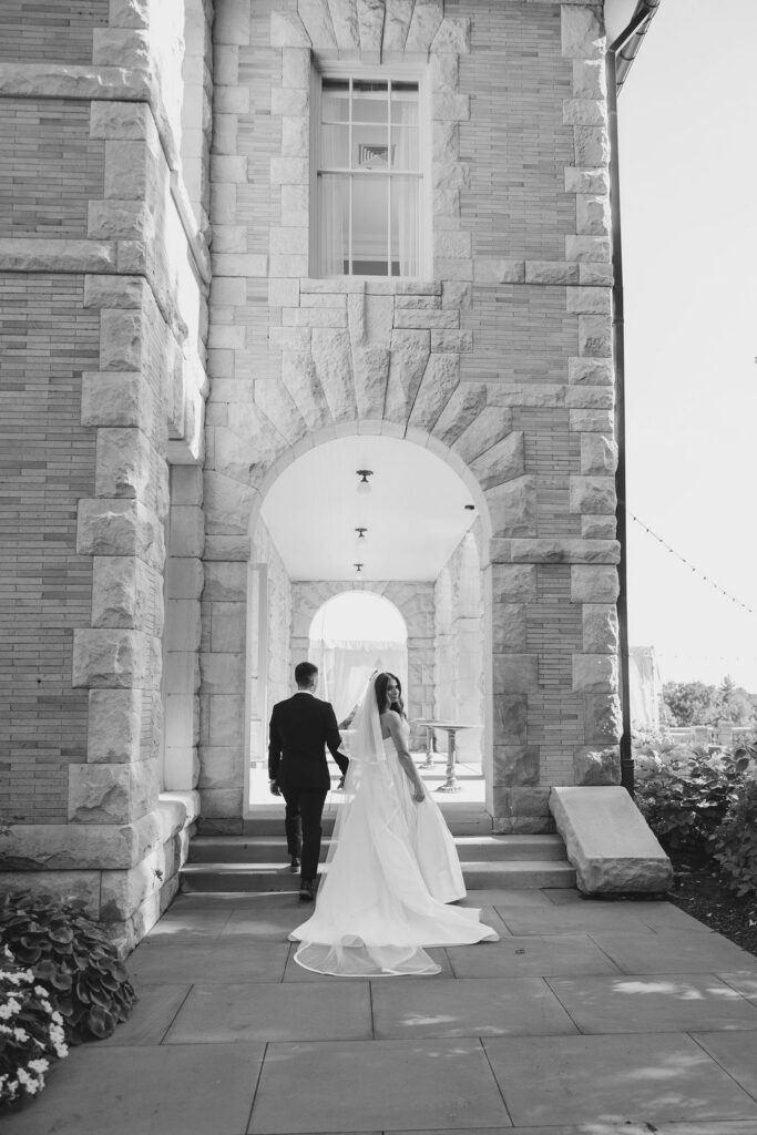 Black and white portrait of bride and groom walking through the stone archway at Cairnwood Estate