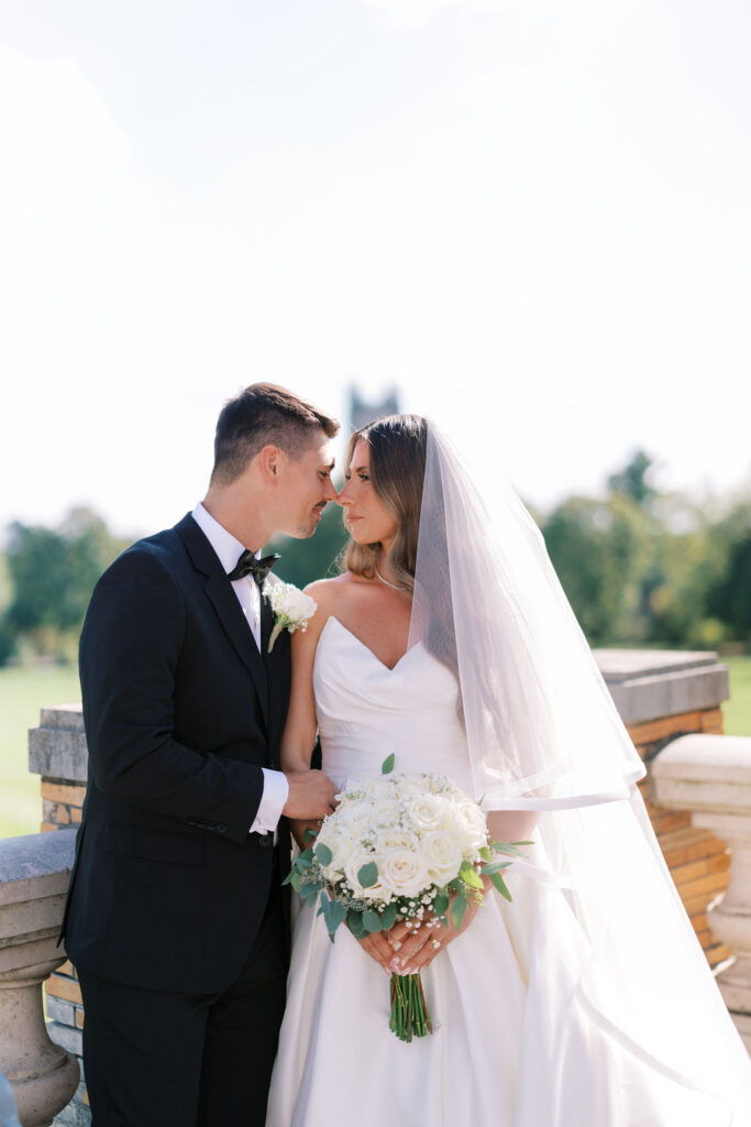 Bride and groom forehead to forehead with white rose bouquet on a terrace