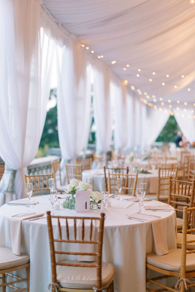 Reception table with gold chiavari chairs, white roses, and Table No. 4 sign at a wedding at Cairnwood Estate