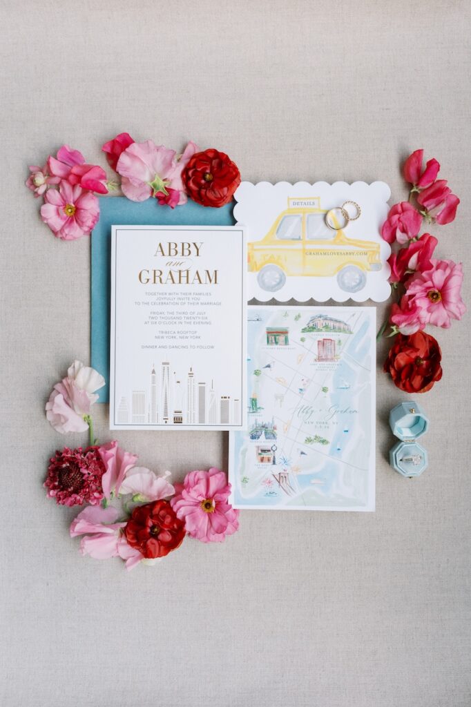 New York City themed wedding invitation suite flat lay surrounded by pink and red flowers arranged by Tribeca Rooftop wedding photographer