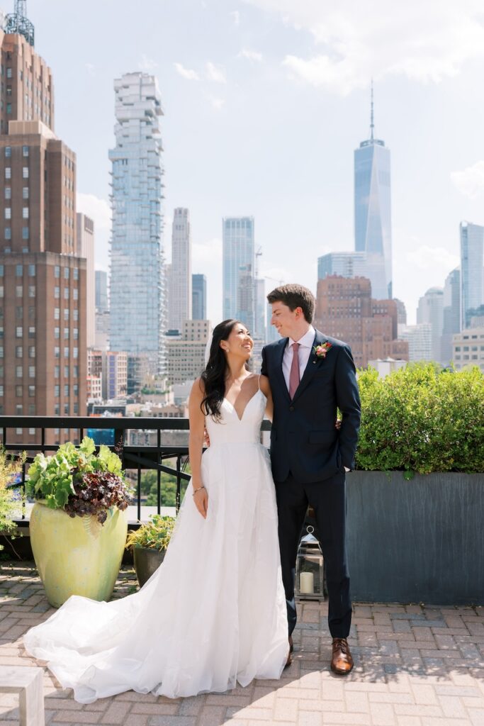 Bride and groom look at each other and smile at Tribeca Rooftop + 360 with the Manhattan skyline in the background