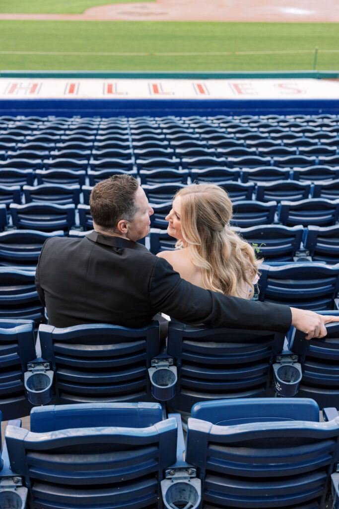 Bride and groom sit in the stands and look at each other smiling at Citizens Bank Park