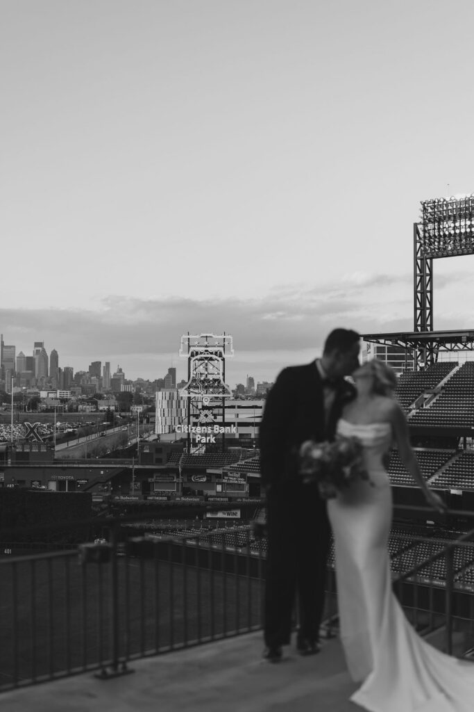 Kissing bride and groom are blurred against the Citizens Bank Park sign in the backdrop glowing in front of the Philadelphia skyline